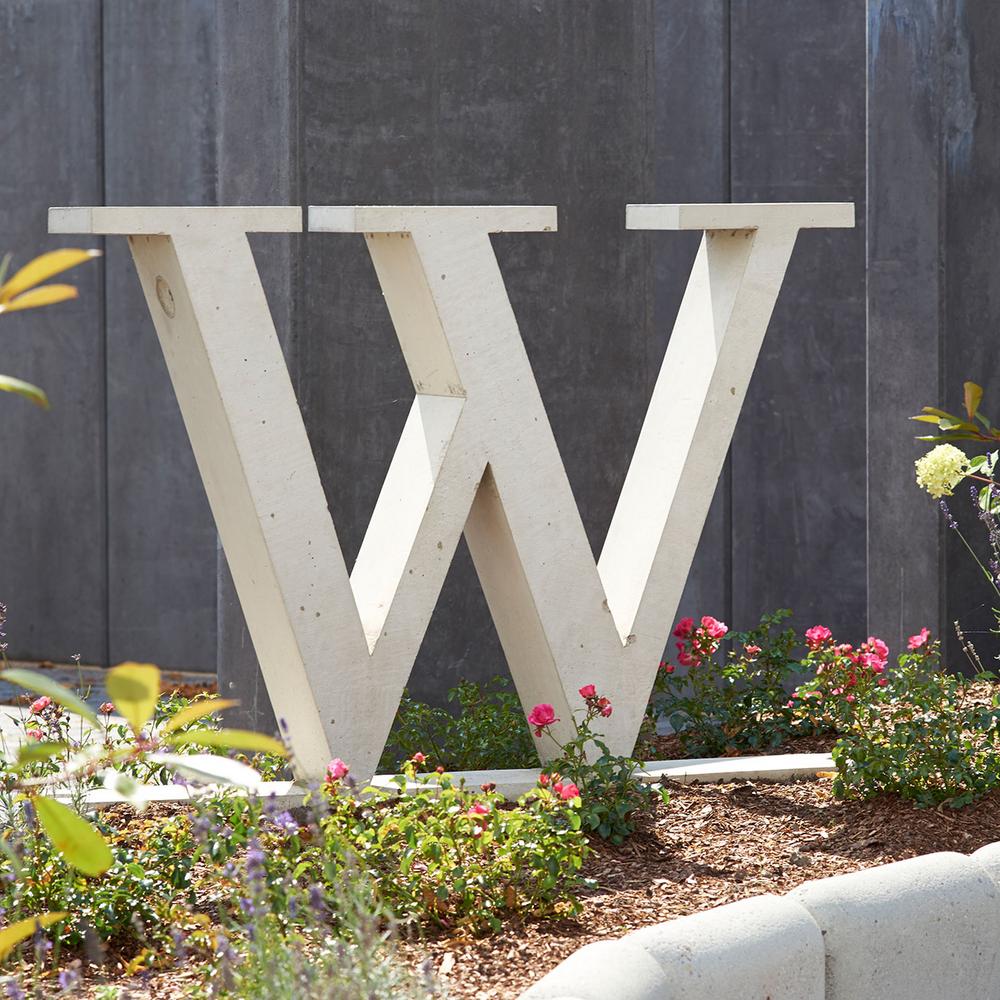 Großer Buchstabe W aus Beton ein einem Blumenbeet