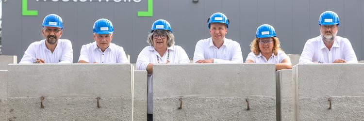 Sechs Mitarbeiter/innen mit Helmen hinter Winkelstützen